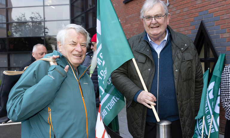 Two men pose for a photo outside the solidarity protest, one holds green NUJ flag