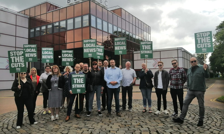 Journalists on picket hold green placards with white text 'Stop the cuts'