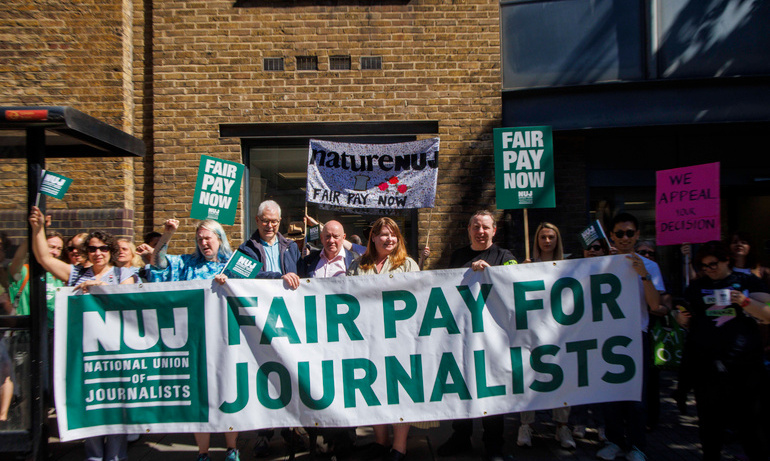 Green and white fair pay now for journalists banner with NUJ logo held by men and women on picket line. Fair pay now placards with white text on green