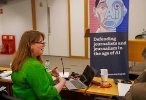 Michelle Stanistreet in green blouse and dark spectacles, pop-up banner with text defending journalism in the age of AI and half robot half human face graphic visible in background.