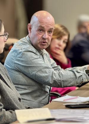 Barry McCaffrey is pictured sitting at desk mid-speech. A woman with a pink coat is pictured in the background.