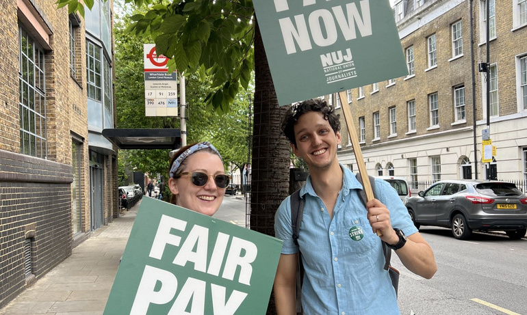 journalists smile as they pose for photo with green placards with text fair pay now in white.
