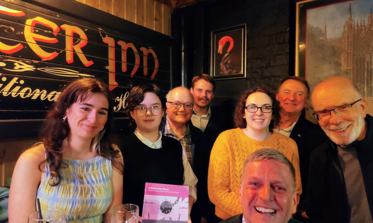 Members smiling in corner of a room, one holds NUJ news recovery plan leaflet