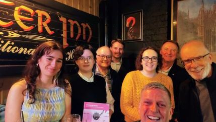 Members smiling in corner of a room, one holds NUJ news recovery plan leaflet